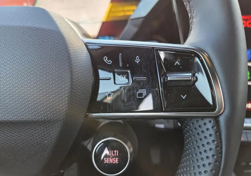 Gros plan sur les commandes du volant textile grainé du Renault Austral 2025, avec bouton MULTI-SENSE éclairé.