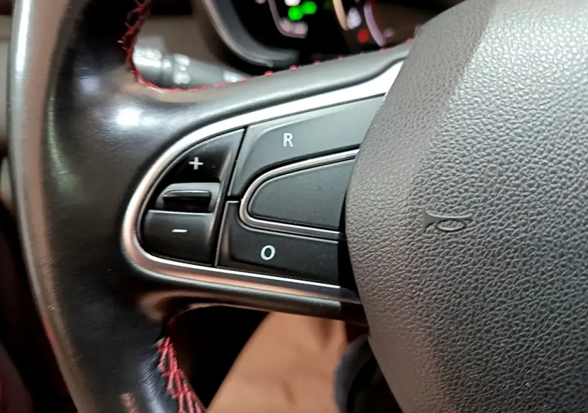 Gros plan sur les commandes de régulateur de vitesse au volant cuir noir avec surpiqûres rouges du Renault Kadjar rouge.