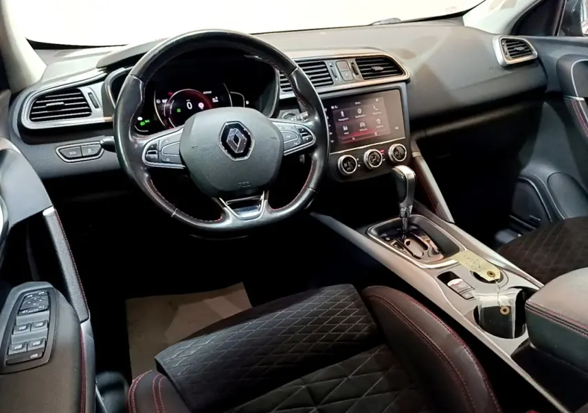 Vue intérieure côté conducteur du Renault Kadjar rouge, mettant en valeur le volant cuir multifonctions et la console centrale avec écran tactile.
