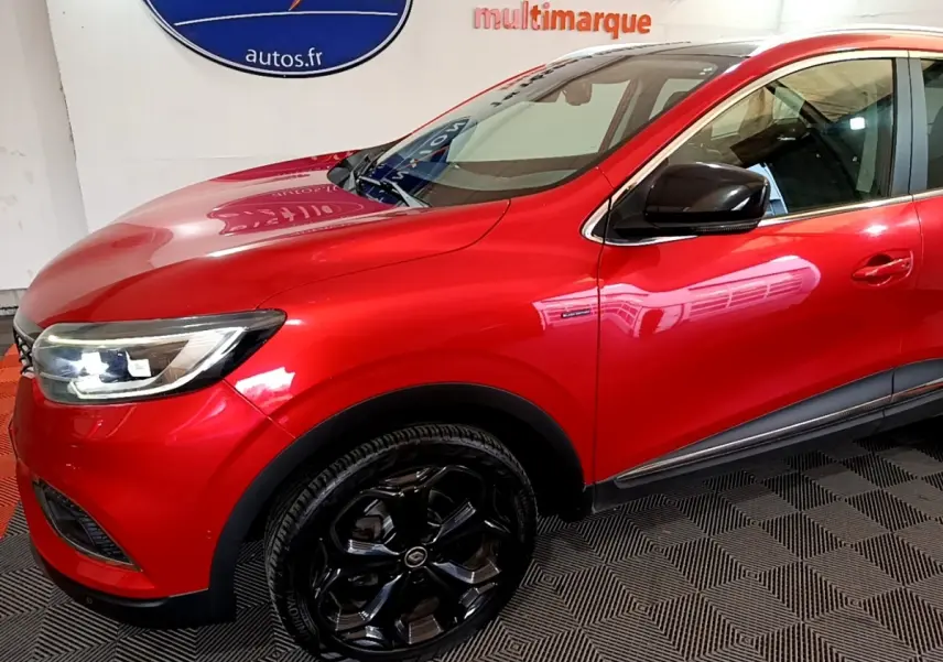 Vue de profil avant droit d’un Renault Kadjar rouge avec jantes noires brillantes et rétroviseur noir.