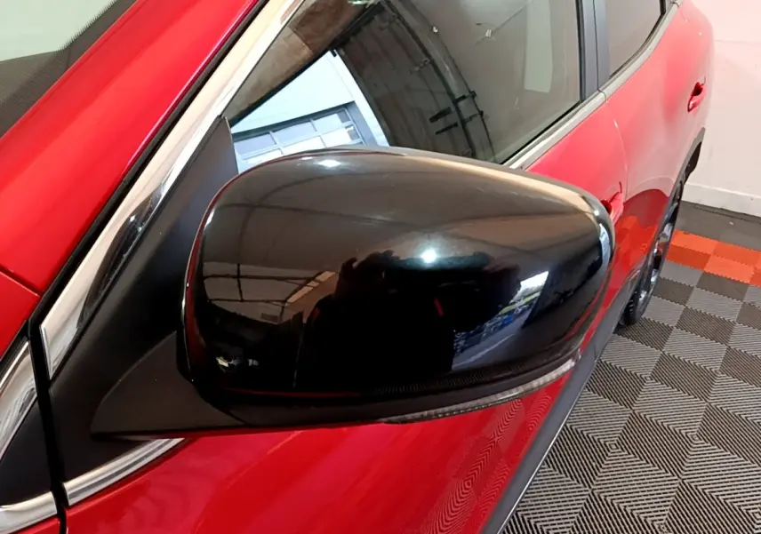 Gros plan sur le rétroviseur noir côté gauche d’un Renault Kadjar rouge, avec reflet de l’environnement intérieur.