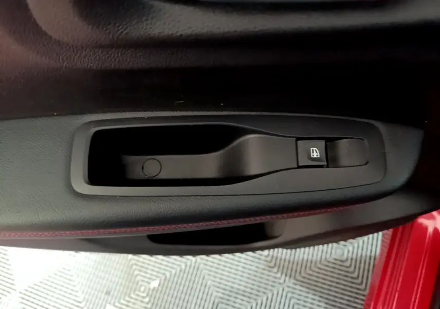 Gros plan sur la poignée intérieure côté gauche d’une Renault Kadjar rouge, avec bouton de commande de vitre électrique.