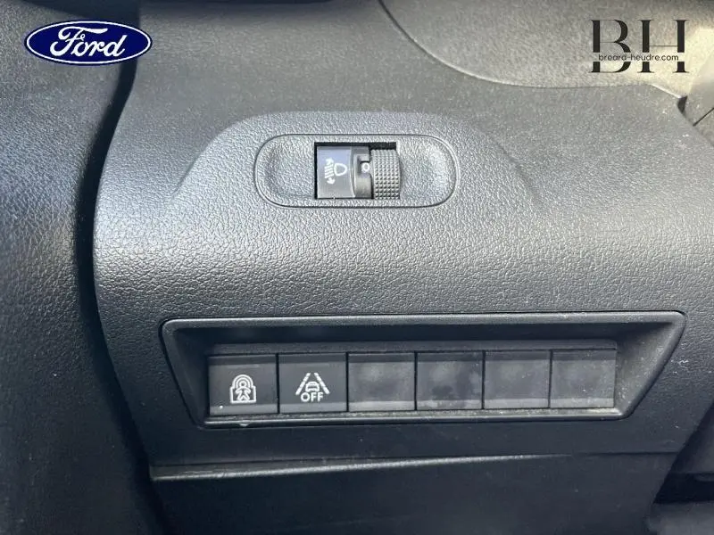Gros plan sur les commandes de réglage des phares et d’aide à la conduite dans un Peugeot Rifter blanc, tableau de bord noir.