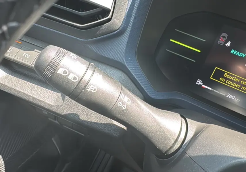 Gros plan sur la commande des feux à gauche du volant du tableau de bord d’un Dacia Duster vert cèdre 2025.