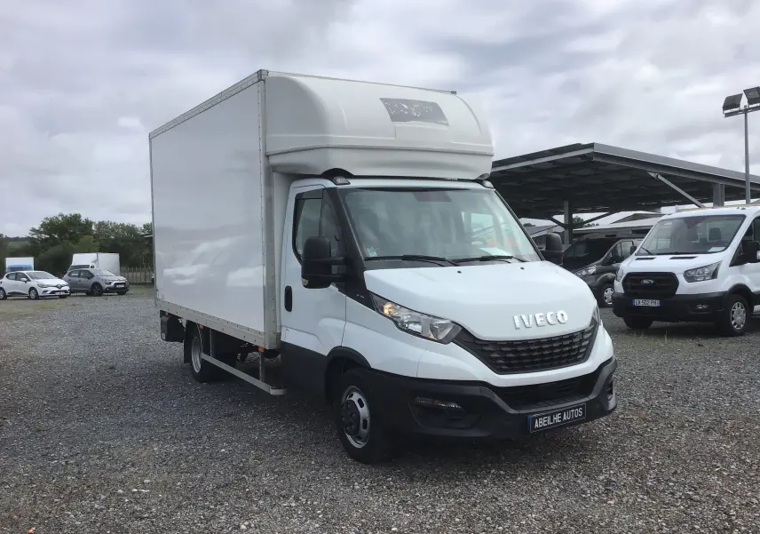 Vue 3/4 avant gauche d'un utilitaire Iveco Daily blanc avec caisse 20m3 et hayon élévateur sur un parking.