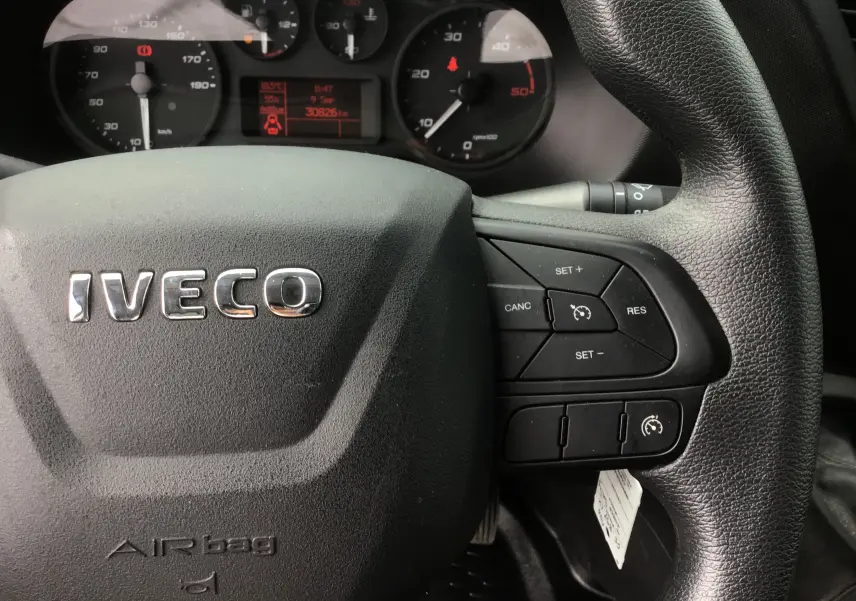 Vue rapprochée du volant noir d'un Iveco Daily 2022 avec commandes de régulateur de vitesse et tableau de bord en arrière-plan.