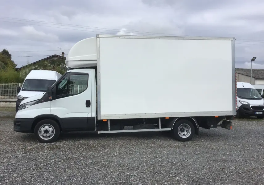Vue latérale gauche d'un utilitaire Iveco Daily blanc avec caisse de 20m3 et hayon élévateur arrière.