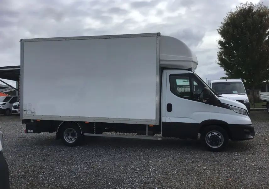 Vue de profil côté gauche d'un Iveco Daily Chassis Cabine blanc avec caisse de 20m3 et hayon arrière sur un sol gravillonné.