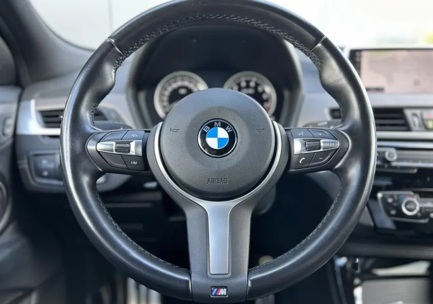 Volant cuir M noir de BMW X2 F39 2021, vue frontale centrée sur le volant avec tableau de bord et écran GPS flous en arrière-plan