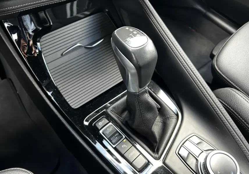 Gros plan sur la console centrale noire du BMW X2 F39, mettant en valeur le levier de vitesses automatique et les boutons de mode de conduite.