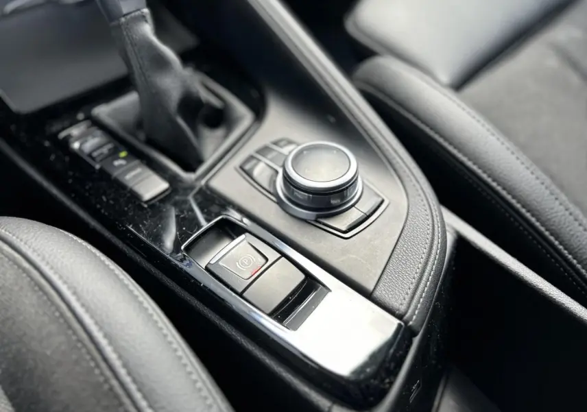 Gros plan sur la console centrale noire du BMW X2 F39, mettant en valeur la commande de frein à main électrique et le sélecteur rotatif.
