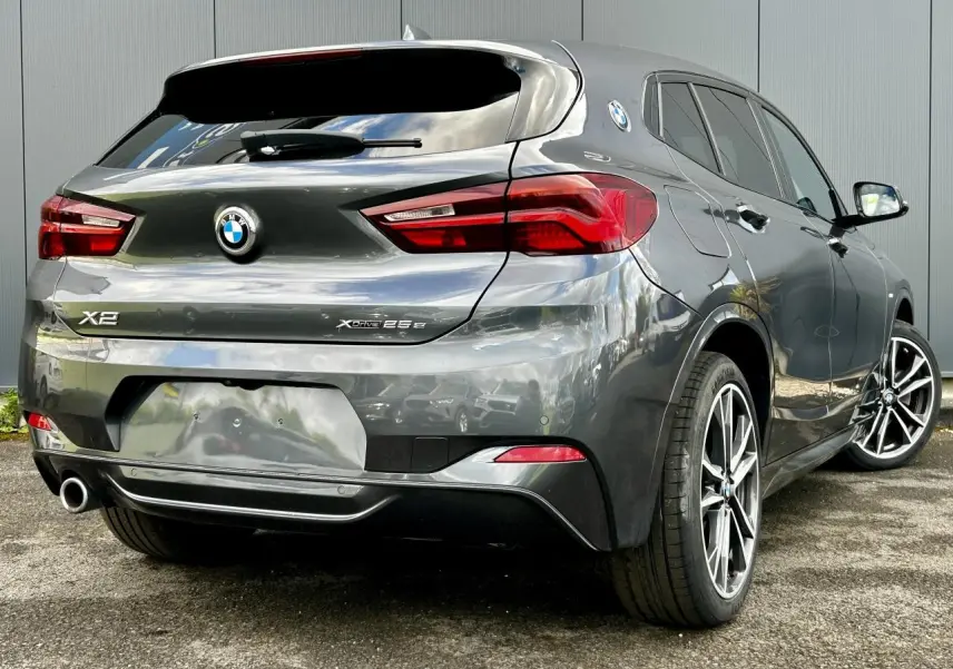 Vue 3/4 arrière droite d'une BMW X2 Gris Mineral avec jantes alliage bicolores et badges xDrive 25e visibles.