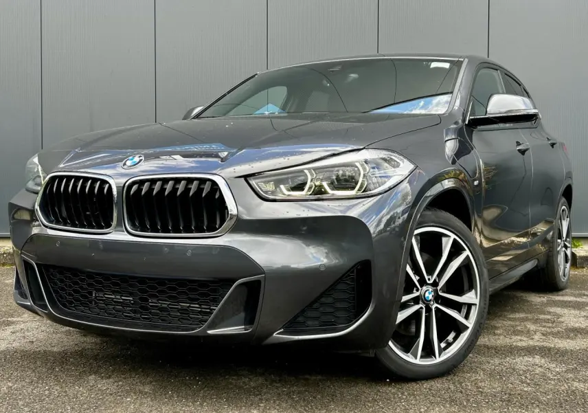 BMW X2 xDrive 25e gris Mineral vue 3/4 avant droit, avec jantes alliage bicolores et calandre M Sport distinctive.