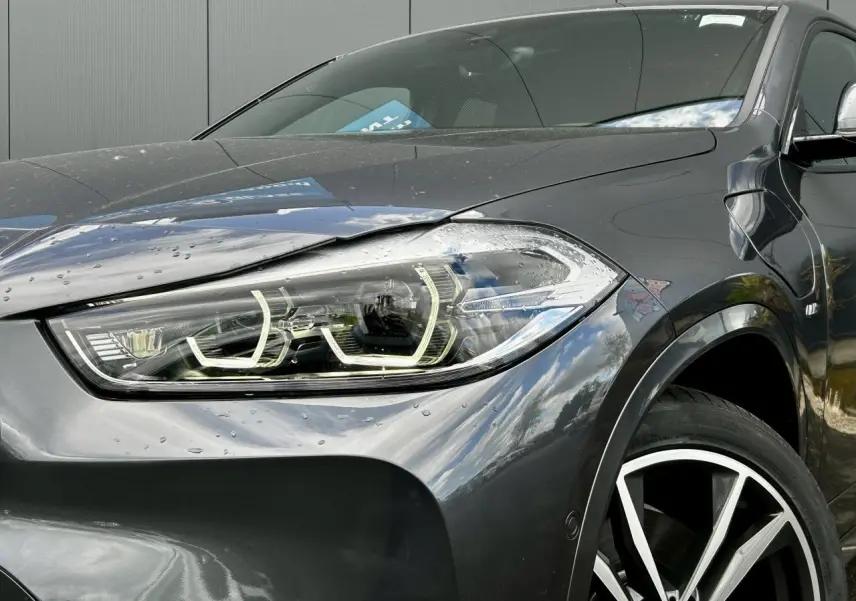 Gros plan sur l'avant droit d'un BMW X2 gris Mineral, mettant en valeur le phare LED et la jante alliage bicolore 19 pouces.