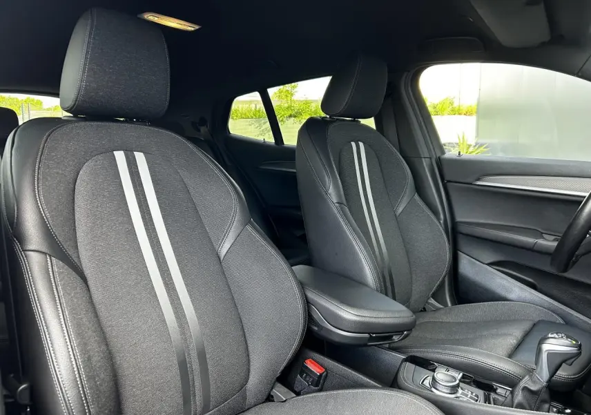 Intérieur de la BMW X2 F39 2021, vue sur les sièges avant noirs avec bandes grises et accoudoir central.