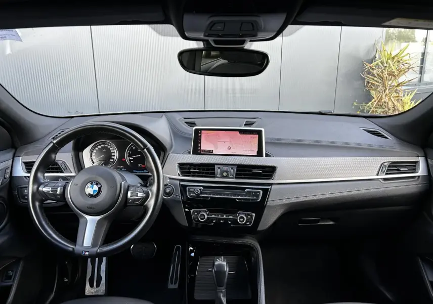 Intérieur BMW X2 F39 2021 vu de face, tableau de bord noir avec écran GPS central et volant M cuir.