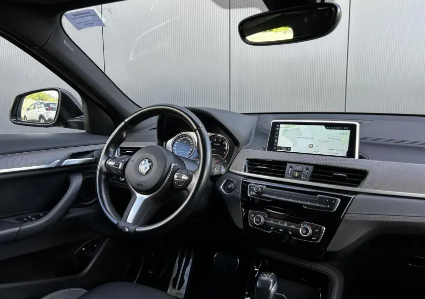 Intérieur BMW X2 F39 vu côté conducteur, tableau de bord noir avec écran GPS et volant M cuir multifonctions.