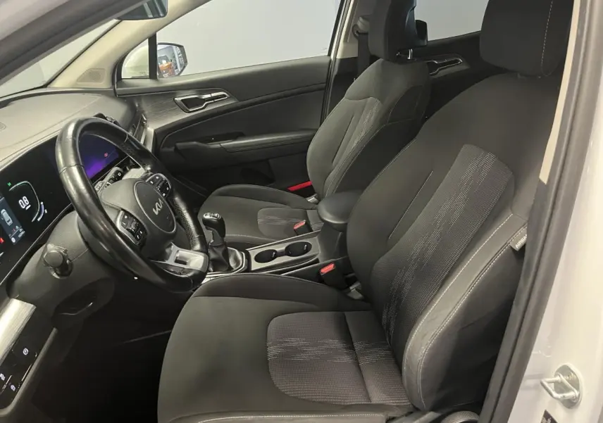 Vue intérieure côté conducteur du Kia Sportage blanc 2022, sièges noirs avec volant cuir et tableau de bord digital.