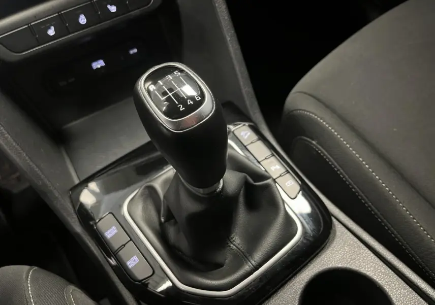 Le levier de vitesses manuel noir du Kia Sportage 2022, entouré de commandes et accoudoir tissu gris.