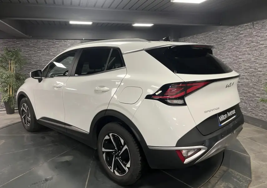 Vue 3/4 arrière droite d'un KIA Sportage blanc nacré avec jantes alliage 18 pouces et feux arrière LED boomerang.