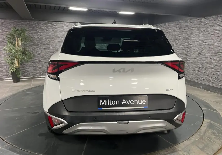 Vue arrière du KIA Sportage blanc nacré avec bouclier noir laqué et feux arrière LED en intérieur showroom.