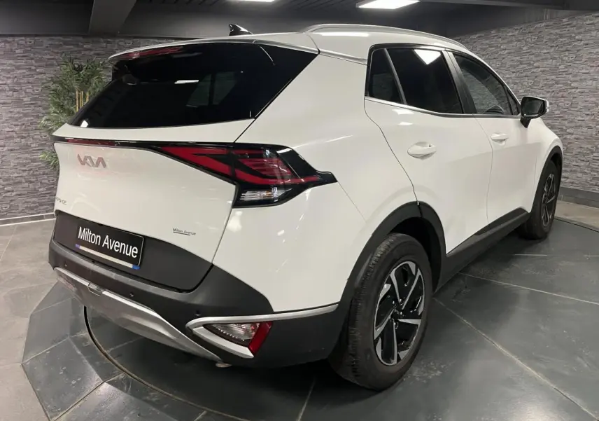 Vue 3/4 arrière droite d'un KIA Sportage blanc nacré avec jantes alliage noires et vitres surteintées.