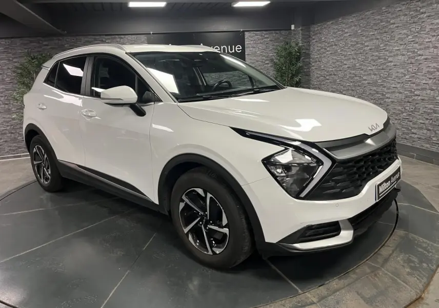 KIA Sportage blanc nacré en 3/4 avant droit, avec calandre noire laquée et jantes alliage 18 pouces.