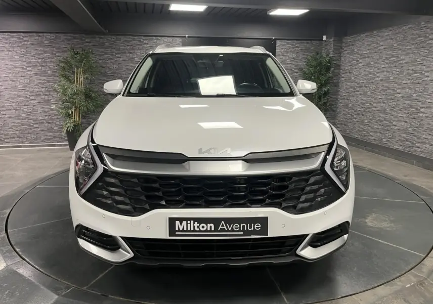 Vue frontale d'un KIA Sportage blanc nacré avec calandre noire laquée et éclairage LED en intérieur showroom.