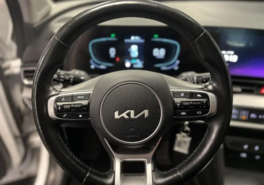 Volant cuir noir du Kia Sportage 2022 avec commandes intégrées et tableau de bord digital en arrière-plan.
