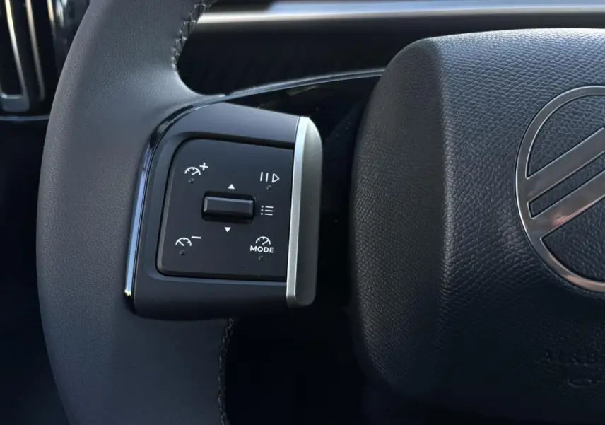 Gros plan sur les commandes multifonctions à gauche du volant noir texturé du Citroën C3 Aircross gris Mercury 2025.