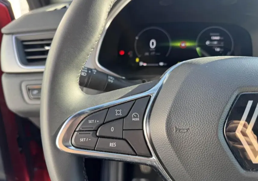 Gros plan sur le volant côté gauche du Renault Captur II Rouge Flamme avec commandes intégrées et tableau de bord numérique flou.