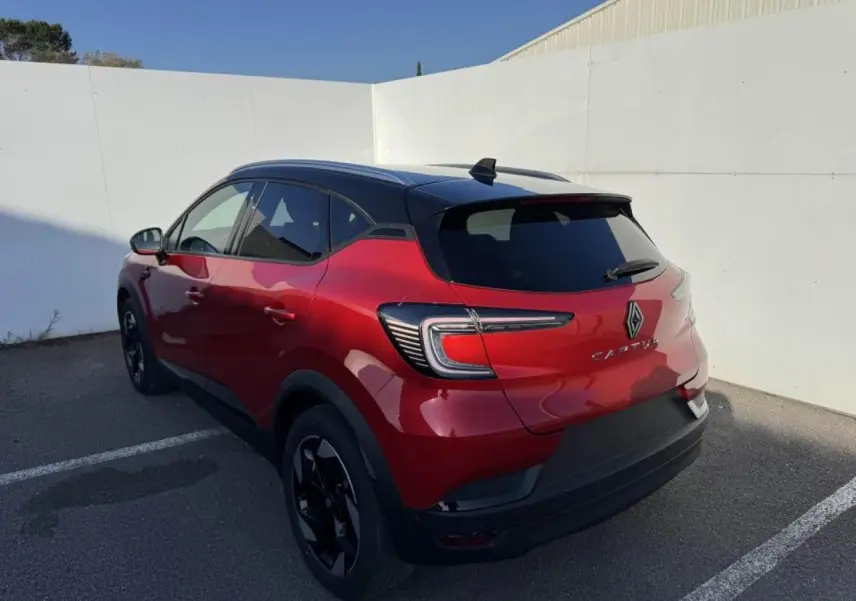Vue 3/4 arrière droite d’un Renault Captur rouge flamme avec toit noir et jantes noires, stationné en extérieur.