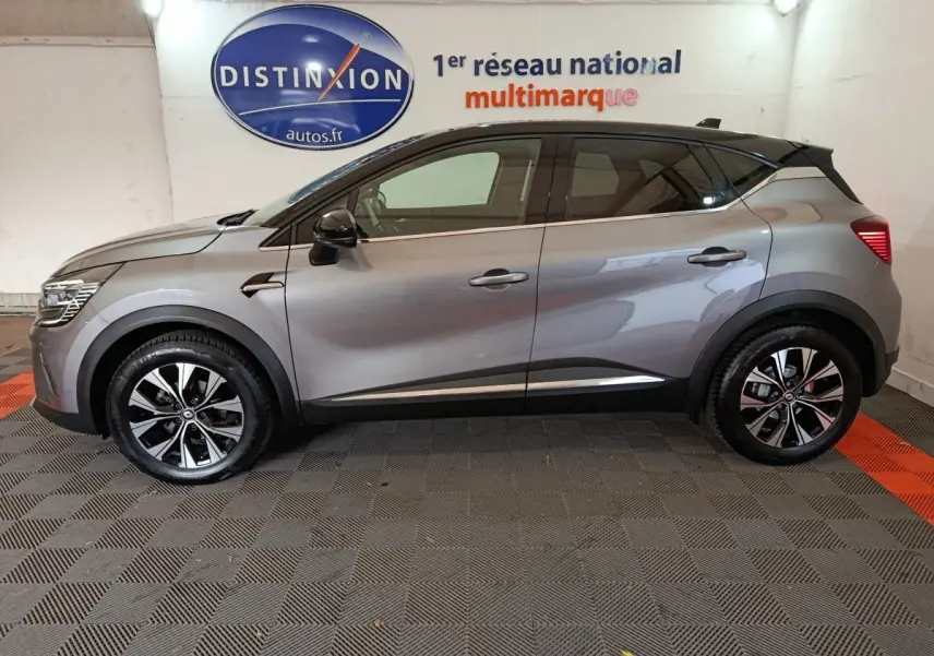 Profil côté gauche d'un Renault Captur Techno TCe 90 gris foncé 2024 avec jantes noires et toit noir contrasté.