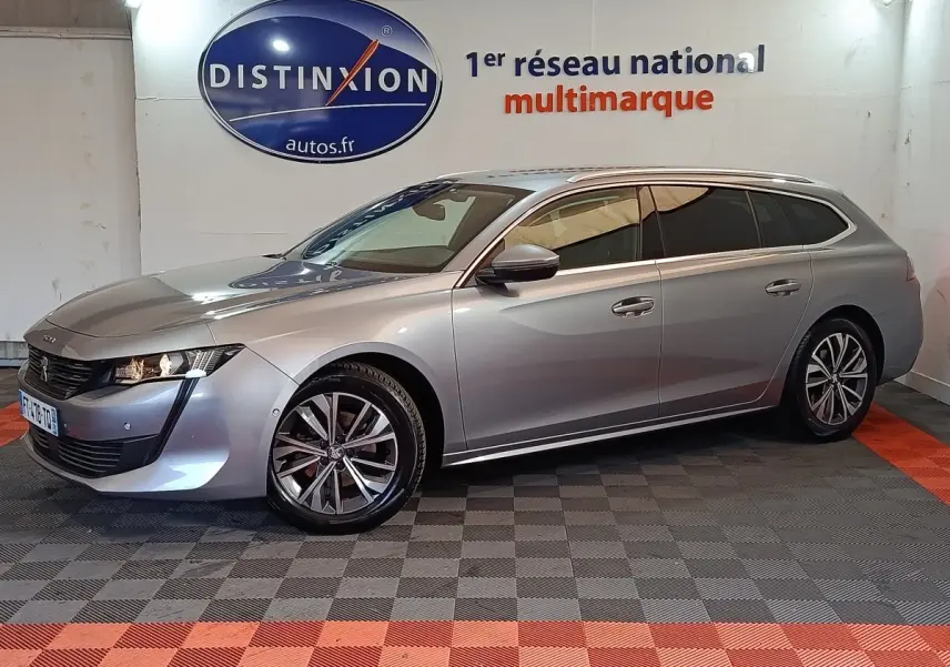 Peugeot 508 break gris clair en 3/4 avant droit, avec jantes alliage et feux LED, stationné en intérieur showroom.