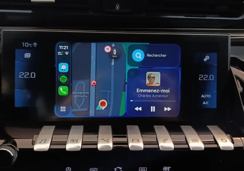 Écran tactile central de la Peugeot 508 gris clair, affichant navigation et musique, avec commandes piano en dessous.