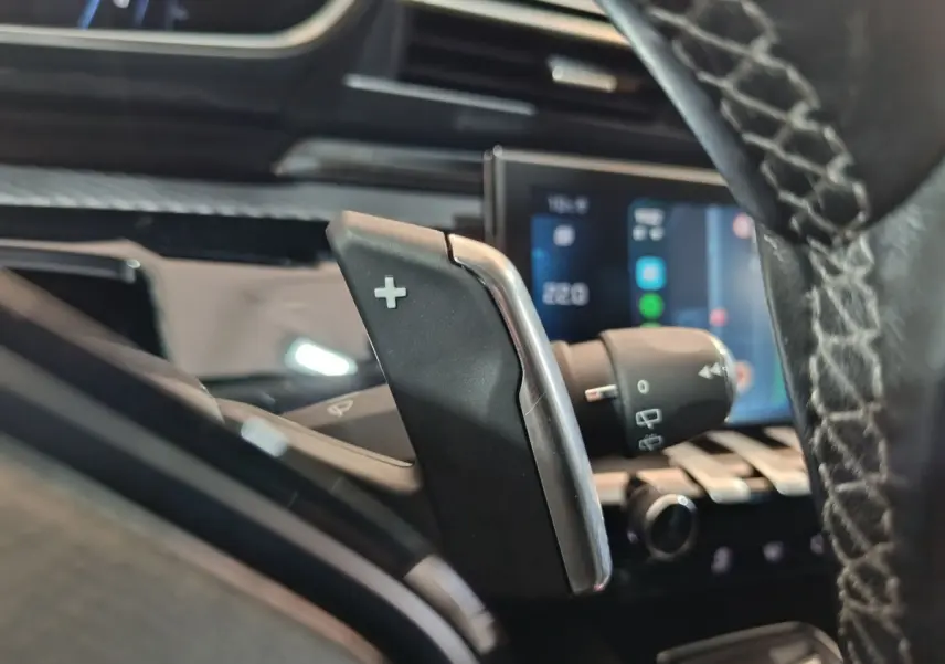 Gros plan sur la palette de changement de vitesse + côté droit du volant cuir de la Peugeot 508 gris clair, tableau de bord tactile en arrière-plan.