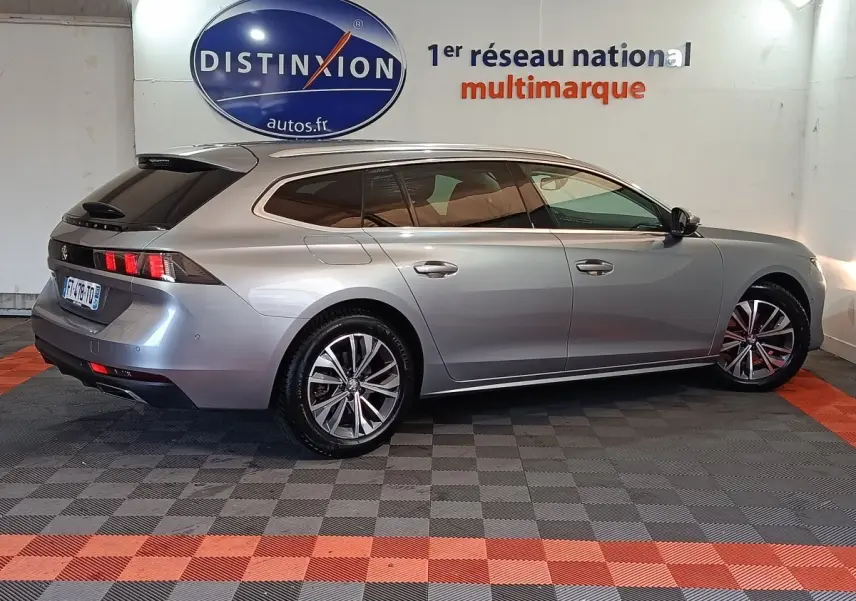 Vue de profil côté droit d’une Peugeot 508 SW gris clair, avec jantes alliage et vitres teintées, en intérieur showroom.