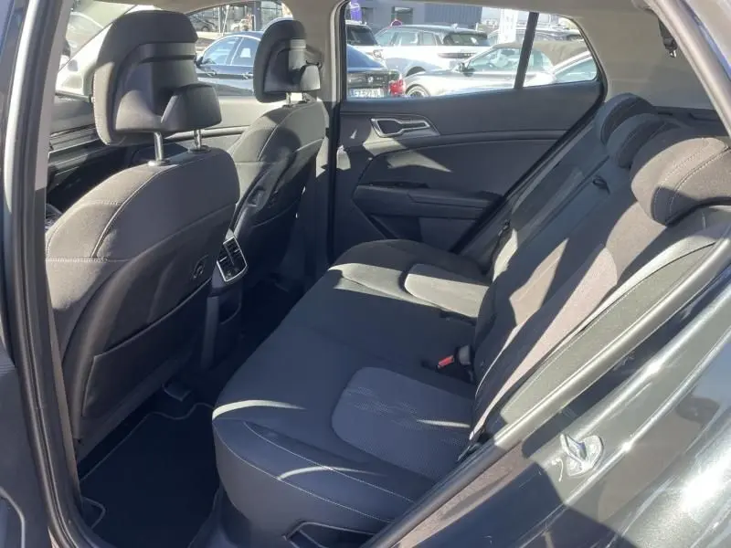 Vue intérieure côté gauche des sièges arrière en tissu noir du Kia Sportage gris Eclipse Metal 2023, avec porte ouverte.