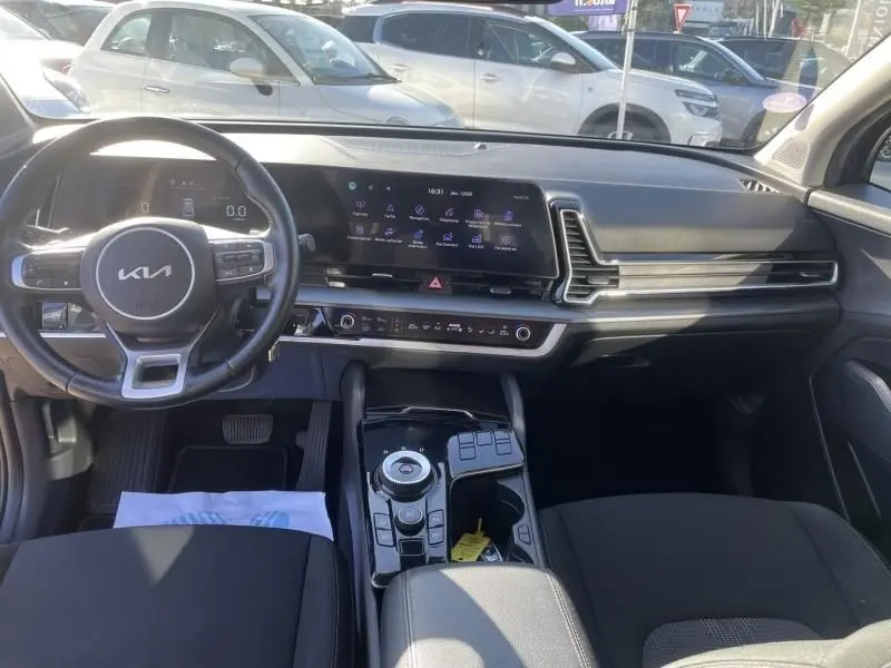 Vue intérieure du tableau de bord et volant noir du Kia Sportage 2023, avec écran tactile large et console centrale moderne.