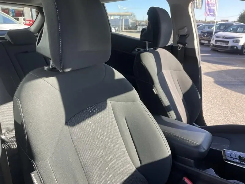 Vue intérieure des sièges avant en tissu noir du Kia Sportage 2023, avec accoudoir central et portière ouverte côté droit.