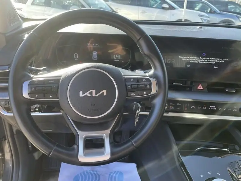 Vue intérieure centrée sur le volant noir du Kia Sportage 2023 avec tableau de bord digital et écran tactile.