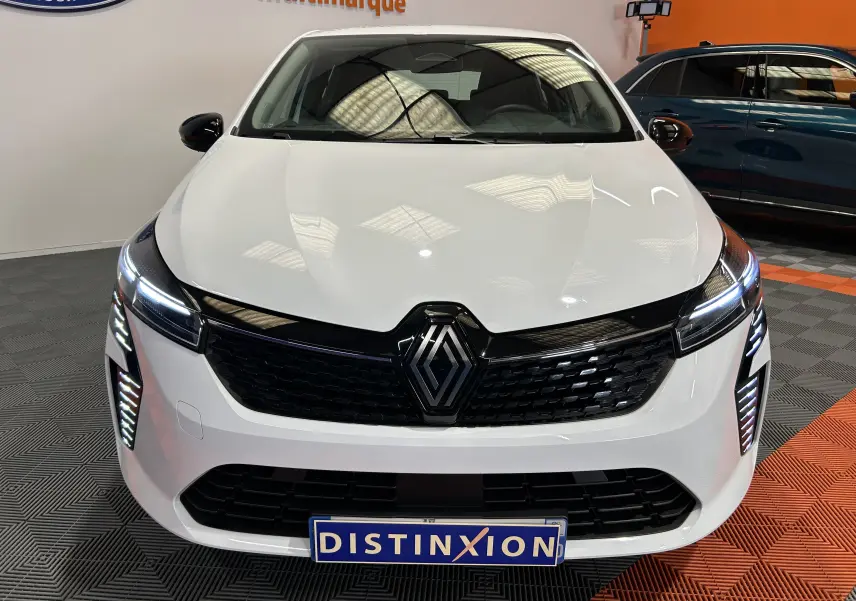 Vue de face d'une Renault Clio V blanche avec calandre noire et feux LED allumés dans un showroom.