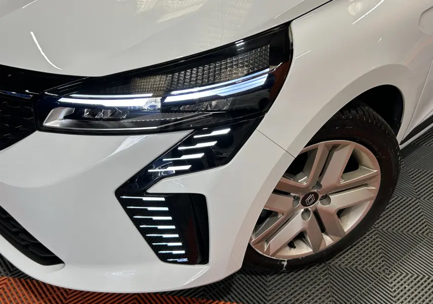 Gros plan sur l'avant droit blanc de la Renault Clio V avec ses feux LED distinctifs et la jante alliage.