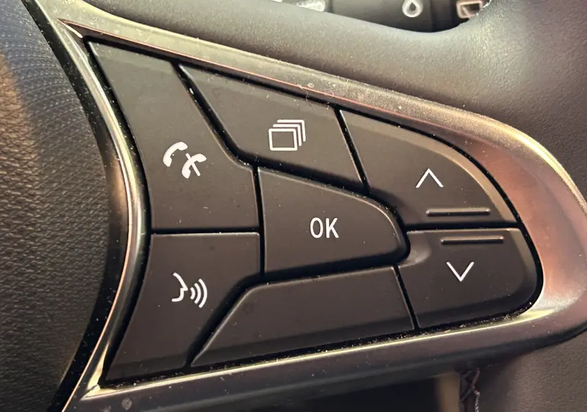 Gros plan sur les commandes multifonctions noires du volant côté gauche d’une Renault Clio V blanche.