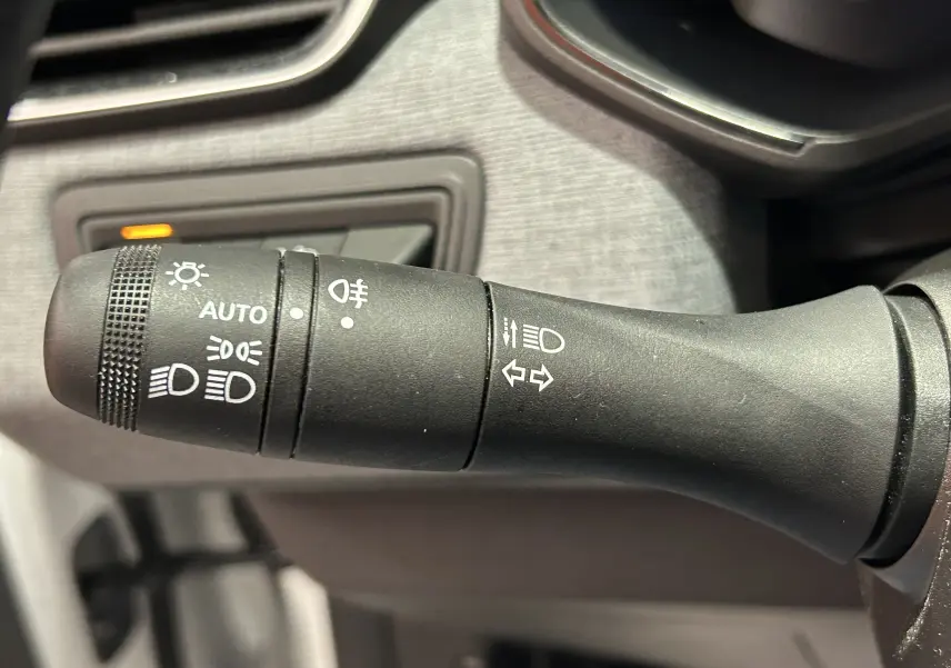 Gros plan sur la commande noire des feux et clignotants du tableau de bord d’une Renault Clio V blanche.