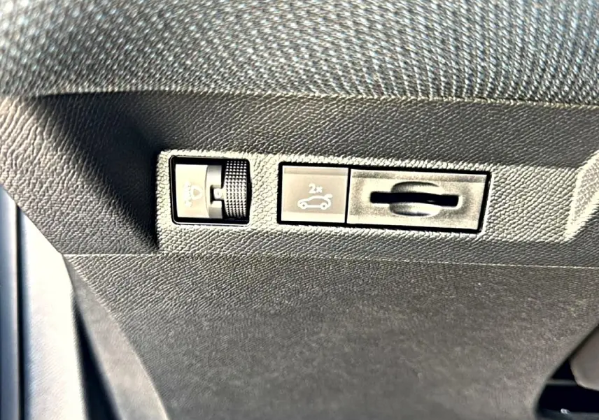 Gros plan sur les commandes sous le tableau de bord du Citroën C5 Aircross gris platinium, bouton ouverture hayon visible.