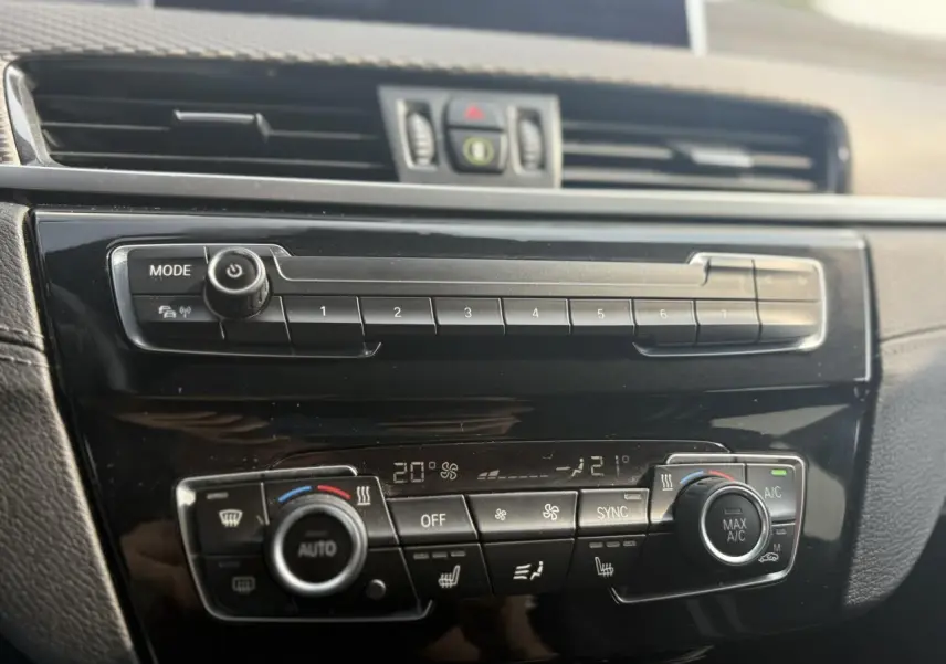 Tableau de bord noir brillant de BMW X2 F39, vue rapprochée sur commandes climatisation automatique et multimédia.