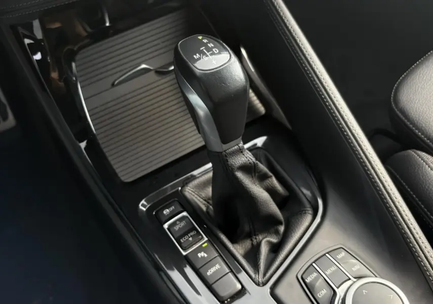 Gros plan sur la console centrale du BMW X2 or Galvanic, avec levier de vitesses automatique et commandes de conduite.