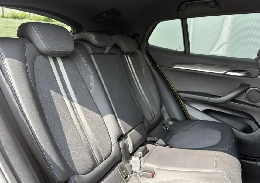 Vue latérale droite de l'intérieur arrière du BMW X2 F39 avec sièges en tissu gris et cuir noir, détails jaunes sur la porte.