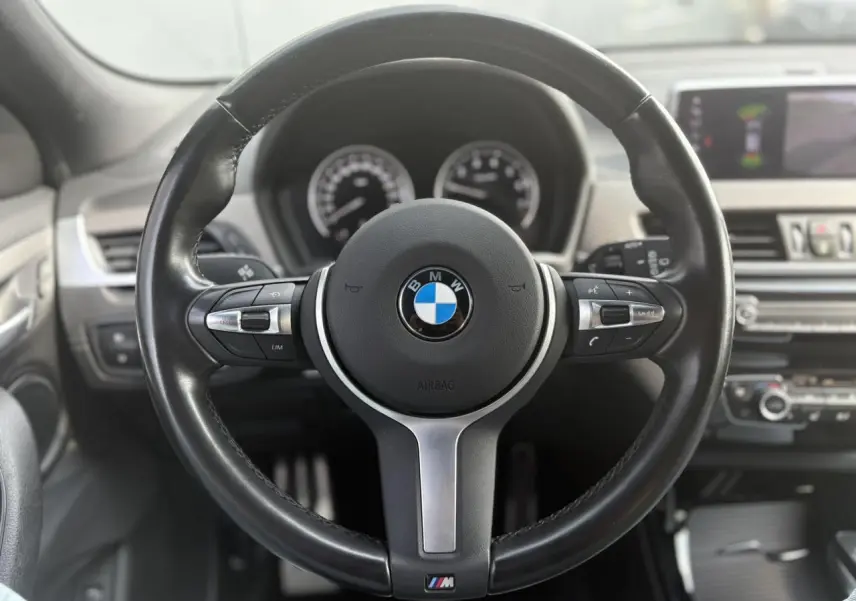 Volant M en cuir noir de BMW X2 F39, vue frontale centrée sur les commandes multifonctions et le tableau de bord flou.